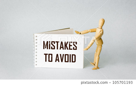 Notepad with text errors to avoid with a wooden doll on a light background. Notepad with text errors to avoid with a wooden doll on a light background. 105701193