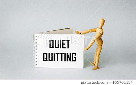 Quiet quitting symbol. Silent care concept words on notepad. Light background. Wooden puppet . 105701194