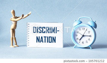 Discrimination - the word is written on a notebook, next to a wooden doll and an alarm clock Discrimination - the word is written on a notebook, next to a wooden doll and an alarm clock 105701212