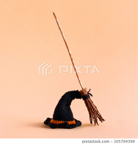 Halloween concept. Black knitted hat and witch's broom on an orange background. 105704399