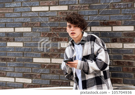 young man with a phone against a brick wall young man with a phone against a brick wall 105704936