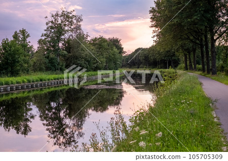 Majestic Purple Sunset: Canal Reflection Amidst Serene Tree-Lined Landscape 105705309