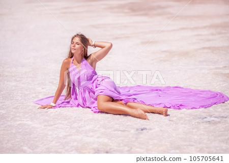 A woman in a pink dress sits on the salty shore of a pink lake and poses for a souvenir photo, creating lasting memories. A woman in a pink dress sits on the salty shore of a pink lake and poses for a souvenir photo, creating lasting memories. 105705641