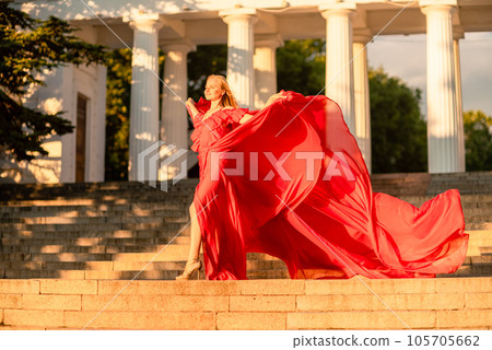 A woman in a long red dress against the backdrop of sunrise, bright golden light of the sun's rays. The concept of femininity, harmony. 105705662