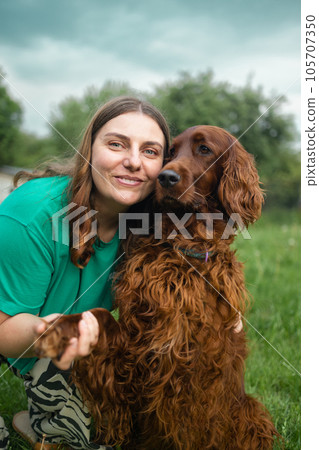 Happy caucasian young redhead woman hugs her beloved Irish Setter dog. Girl and dog in the spring forest at sunset Happy caucasian young redhead woman hugs her beloved Irish Setter dog. Girl and dog in the spring forest at sunset 105707350