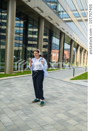 Beautiful woman using mobile phone while listening voice note with wireless earbuds choosing radio podcast e-book online relaxing in a city street.  105707408
