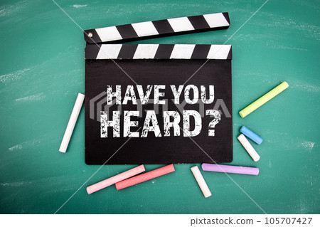 Have You Heard. Black movie clapper with chalk pieces on a green chalkboard background Have You Heard. Black movie clapper with chalk pieces on a green chalkboard background 105707427