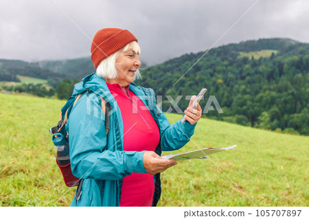 Happy senior woman with map hiking in woods. Adventure women pointing finger on mountains background.  105707897