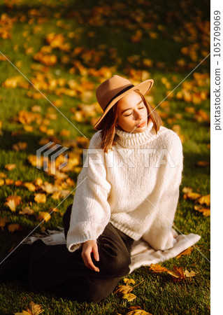 Autumn woman. Young cheerful woman in white sweater and hat walks in the nature park on a sunset. 105709069