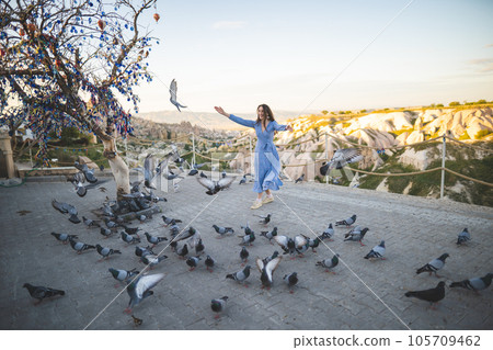 a beautiful and happy girl in a dress and many pigeons in the mountains of Cappadocia a beautiful and happy girl in a dress and many pigeons in the mountains of Cappadocia 105709462