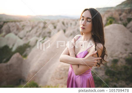 a beautiful girl in a long pink dress poses at sunset in the mountains of Cappadocia 105709478
