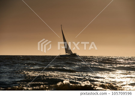 The view of sailboat is heeling at sunset, reflection of sun on water surface The view of sailboat is heeling at sunset, reflection of sun on water surface 105709596