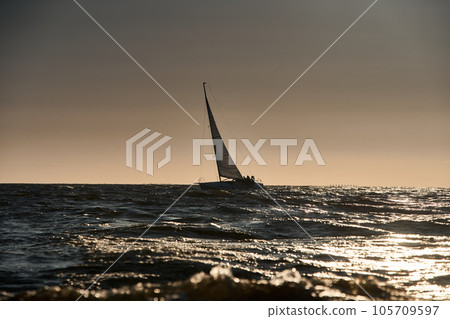 The view of sailboat is heeling at sunset, reflection of sun on water surface 105709597