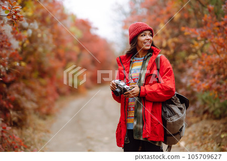 Beautiful woman taking pictures in autumn forest. Smiling woman enjoying autumn weather. Lifestyle 105709627