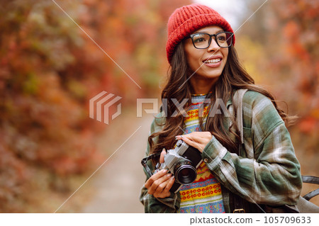 Beautiful woman taking pictures in autumn forest. Smiling woman enjoying autumn weather. Lifestyle 105709633