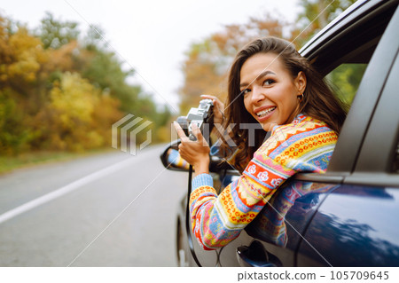 Beautiful woman takes pictures on camera from the car window. Rest, relaxation, lifestyle concept. 105709645