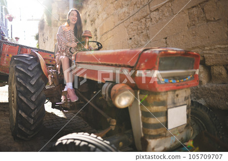 A beautiful girl in a dress rides an old tractor 105709707