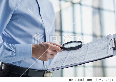 Businessman looking through a magnifying glass to documents 105709843