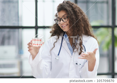 Young pharmacist woman holding pills while sitting at the table in the office Young pharmacist woman holding pills while sitting at the table in the office 105709870