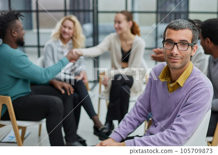 A happy young businessman, in a purple sweater, sits against the background of his colleagues 105709873