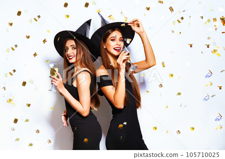 portrait of two happy young women in black witch halloween costumes on party over white background. 105710025
