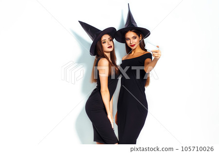 portrait of two happy young women in black witch halloween costumes on party over white background. 105710026