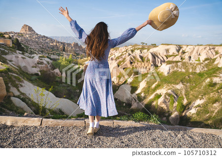 a beautiful girl in a dress and hat is enjoying the mountain landscape in Cappadocia 105710312