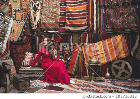 a beautiful girl in a red dress in a traditional turkish interior with many carpets on the wall a beautiful girl in a red dress in a traditional turkish interior with many carpets on the wall 105710318