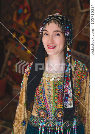 beautiful girl dressed in Turkish national clothes in the room with the interior there are many carpets on the walls beautiful girl dressed in Turkish national clothes in the room with the interior there are many carpets on the walls 105710354