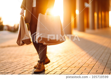 Shopping bags in the hands at sunset. Hand of young man with paper bags with purchases. 105710599