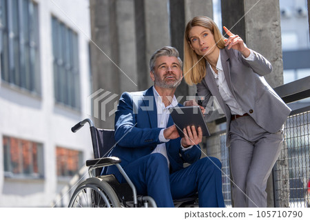 Woman and man in wheelchair working together, joint architecture project, using laptop and tablet. 105710790