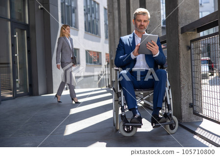 Executive business man in wheelchair with tablet using mobile device for work outdoors. 105710800