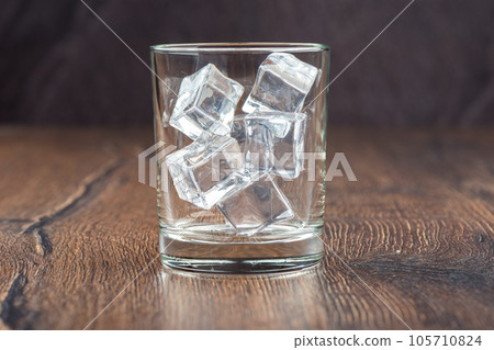 Ice cubes in an empty glass on a wooden bar counter, dark background. 105710824