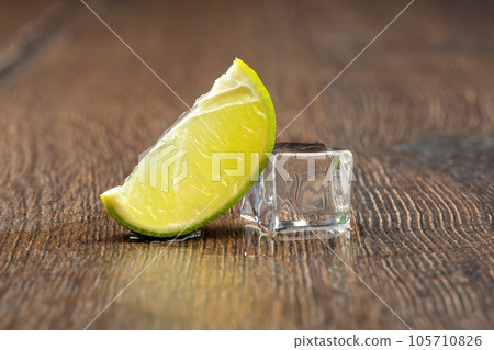 Slice of lime and a melting ice cube with drops of water on the table. 105710826