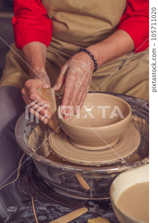 Hands of mature woman master of ceramics working on a potter's wheel, making plate of clay in art studio. Hands of mature woman master of ceramics working on a potter's wheel, making plate of clay in art studio. 105711020