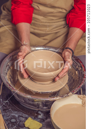Hands of mature woman master of ceramics working on a potter's wheel, making plate of clay in art studio. Hands of mature woman master of ceramics working on a potter's wheel, making plate of clay in art studio. 105711023