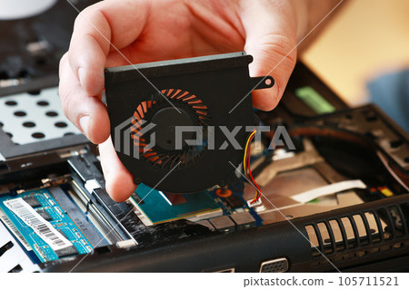 Fixing laptop. Repairman holds cooling fan and repairs from overheating. Disassembling computer, replacement, clean dust and dirt cooling system on notebook. Professional electronic device service Fixing laptop. Repairman holds cooling fan and repairs from overheating. Disassembling computer, replacement, clean dust and dirt cooling system on notebook. Professional electronic device service 105711521