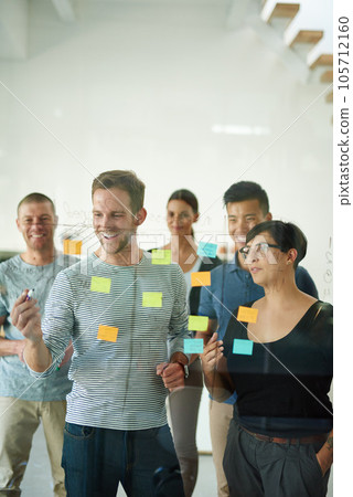 Confident manager, leader or boss talking in a meeting, workshop or presentation with sticky notes in the boardroom. Businessman talking, discussing and brainstorming with a group of colleagues 105712160