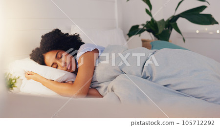 Young black woman sleeping in bed in her bedroom while resting and having a dream at home. Relax, peaceful and calm African girl taking a nap with a comfortable pillow and blanket at her house. 105712292