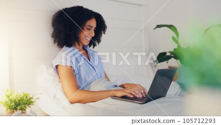 Blog writer typing with laptop for internet streaming website and reading funny social media post in bed at home. Woman freelance worker in bedroom working remote while writing funny or comic web con 105712293