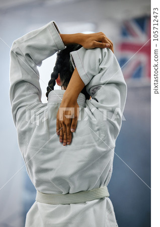 Person doing a warmup, stretching or exercising before doing karate, judo or taekwondo at a gym alone from behind. Back view of an instructor or trainer in martial arts doing stretches before a class Person doing a warmup, stretching or exercising before doing karate, judo or taekwondo at a gym alone from behind. Back view of an instructor or trainer in martial arts doing stretches before a class 105712473