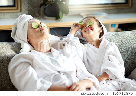 Fresh skincare, face mask and healthy skin treatment for bonding mother and daughter home spa day. Fun, smiling and playful child and parent relaxing with cucumber over their eyes in grooming routine 105712870