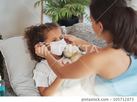 Health care for sick, tired little girl with covid wearing face mask while resting on a sofa at home with worried mother. Anxious parent helping her unwell daughter to protect and stop virus spread Health care for sick, tired little girl with covid wearing face mask while resting on a sofa at home with worried mother. Anxious parent helping her unwell daughter to protect and stop virus spread 105712873