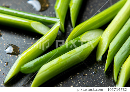 A close-up of a cooking scene in which garlic sprouts (diagonally cut) are fried in a frying pan. 105714782