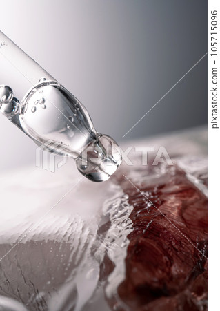Pipette on a large piece of ice with frozen flowers. 105715096