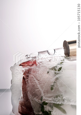 Pipette on a large piece of ice with frozen flowers. 105715130