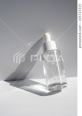 A white transparent bottle with serum in the rays of the sun. 105715335