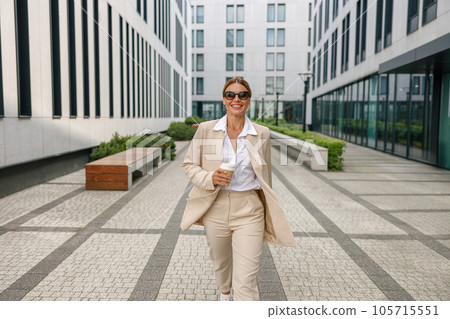 Smiling business woman with coffee walking on modern building background during break time 105715551