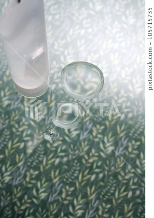 A transparent bottle of cosmetic gel on a green background with drops of the product. A transparent bottle of cosmetic gel on a green background with drops of the product. 105715735