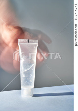 A transparent bottle of cosmetic gel with a blurred hand on the background. A transparent bottle of cosmetic gel with a blurred hand on the background. 105715741